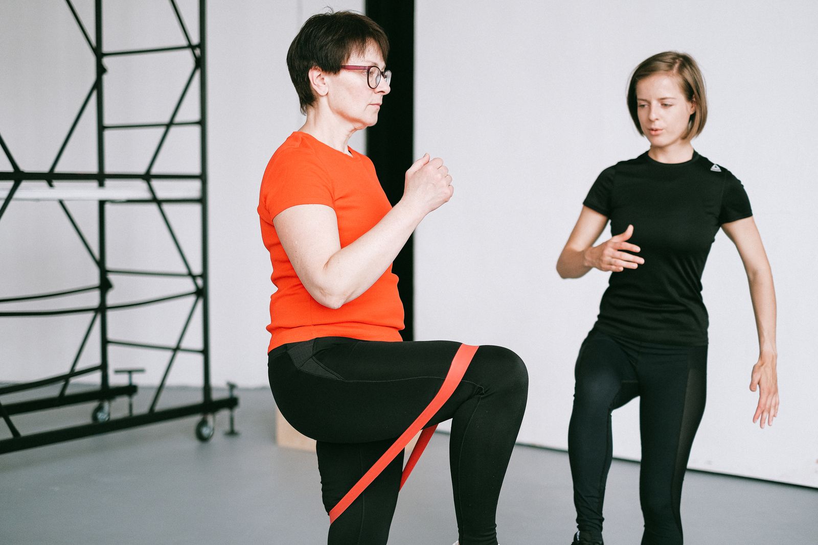 Entraîneur personnel guidant une femme avec un exercice de bande de résistance dans un cadre de gym.